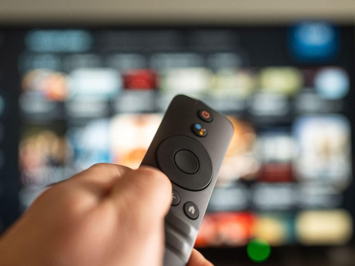 Person hält eine Fernbedienung auf einen eingeschalteten Fernseher