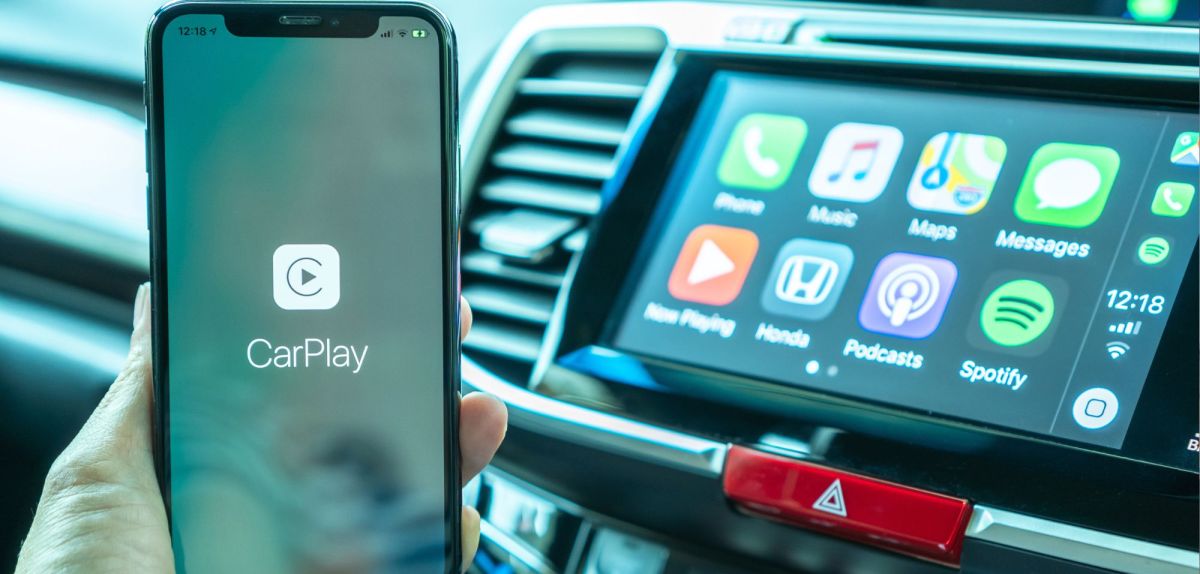 Person sitzt in einem Auto und bedient Apple Carplay an einem iPhone.