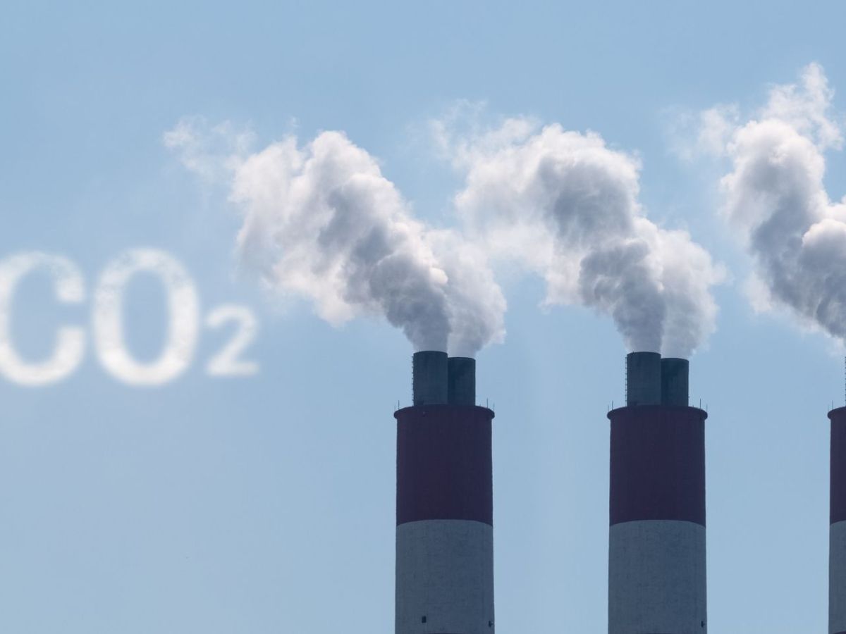 Drei Industrieschornsteine, aus denen Rauch kommt. Daneben steht in der Farbe des Rauchs CO2.