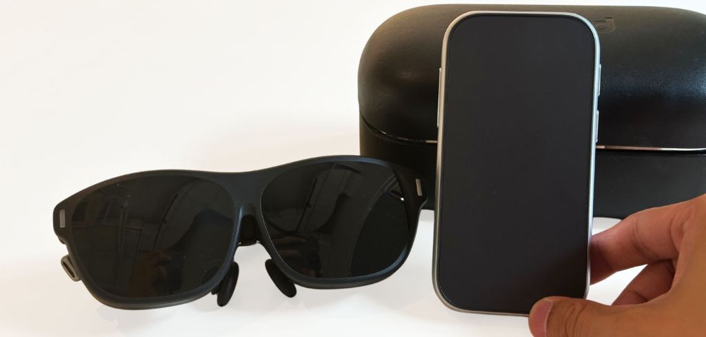 Nahaufnahme eines Rokid-AR-Brillen-Sets: schwarze AR-Sonnenbrille, ein handgroßer silberner Controller / Hub (Rokid Station) und ein passendes schwarzes Etui vor weißem Hintergrund.
