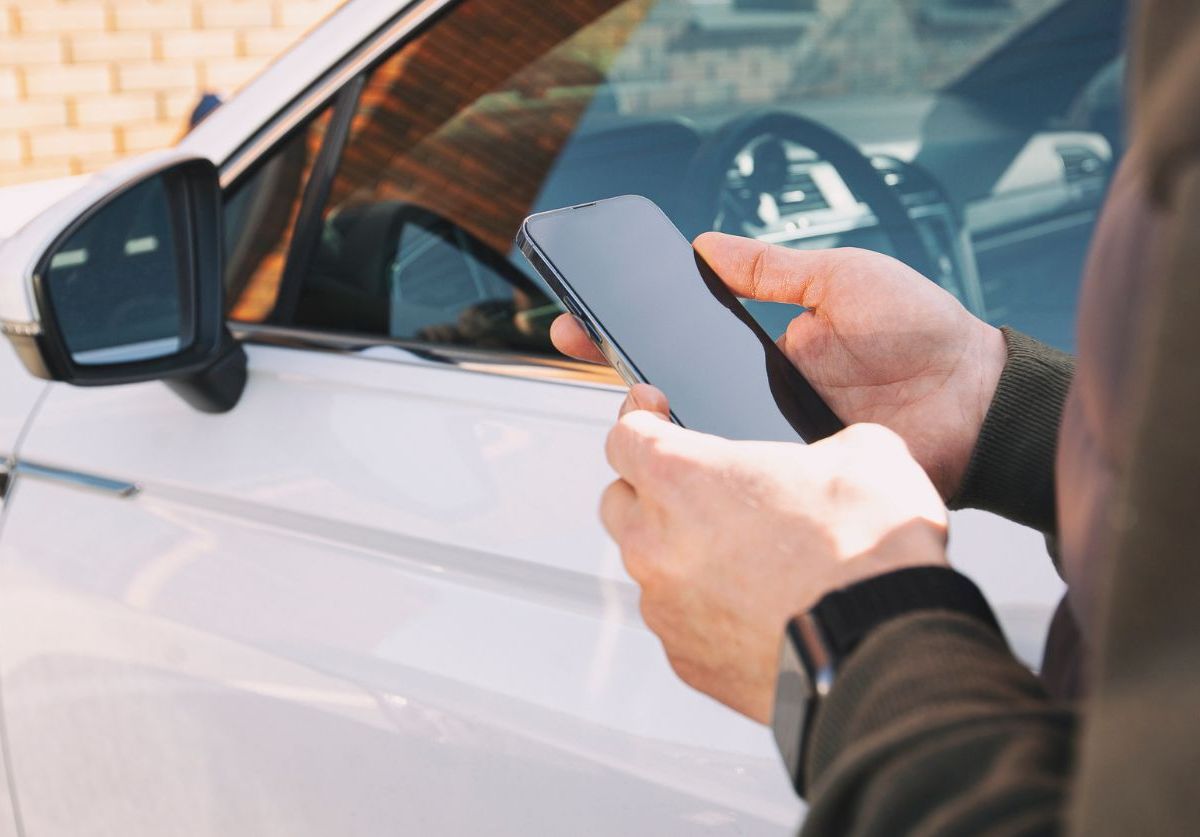 Person steht mit Smartphone in der Hand vor einem Auto.