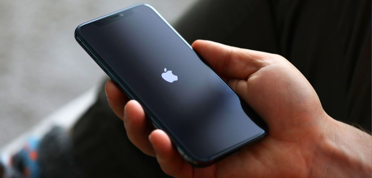 Person hält ein iPhone in der Hand. Auf dem Display ist das Apple-Logo zu sehen.