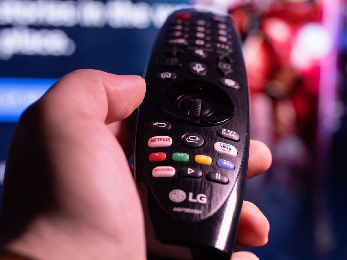 Person hält eine Fernbedienung in der Hand, die in Richtung eines Fernsehers zeigt.
