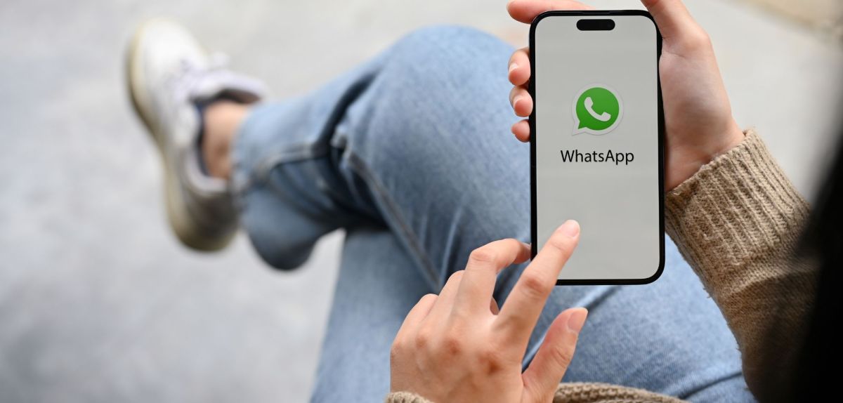 Person hält Handy mit WhatsApp darauf hoch.