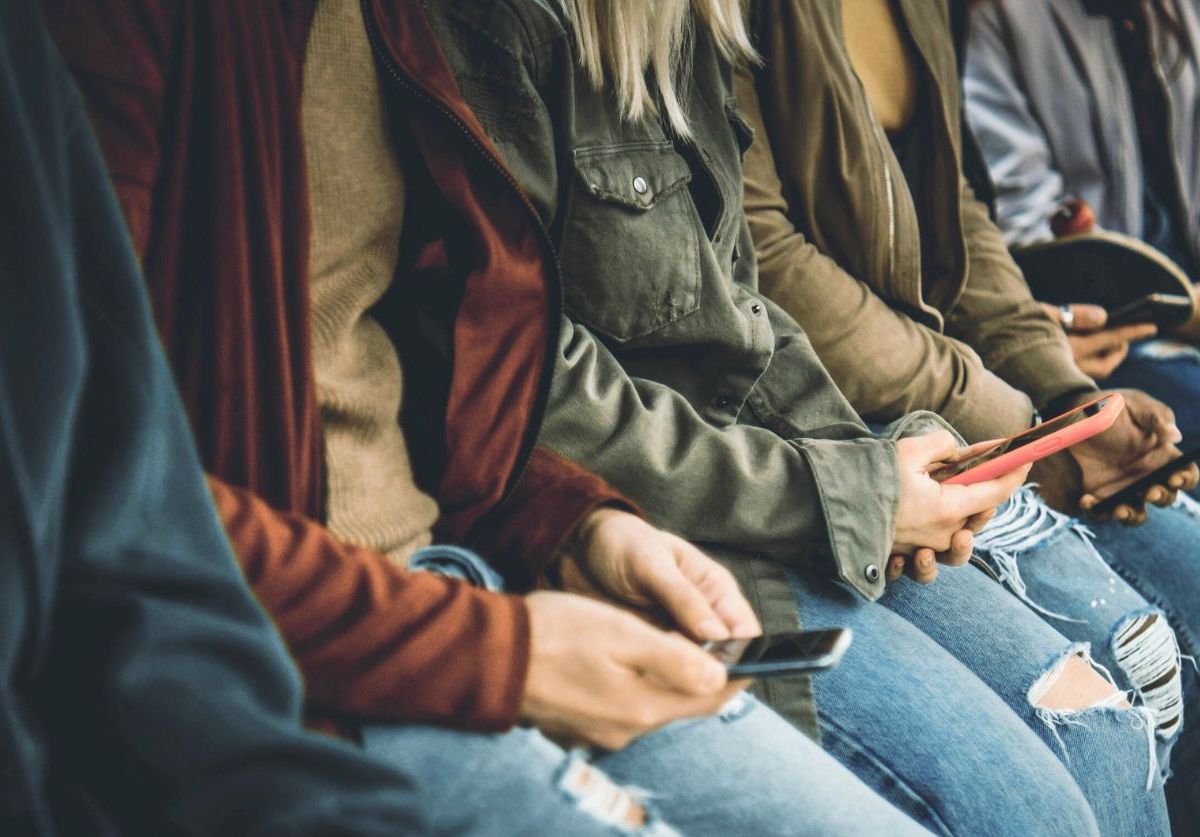 Personen sitzen jeweils mit einem Smartphone in der Hand nebeneinander.