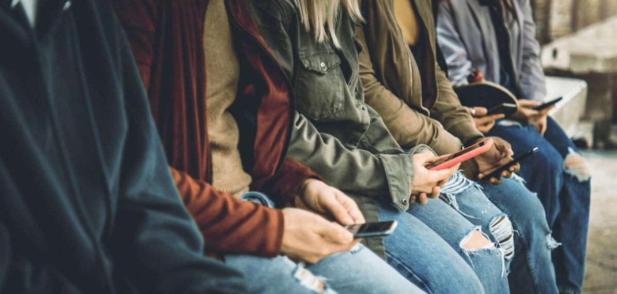Personen sitzen jeweils mit einem Smartphone in der Hand nebeneinander.