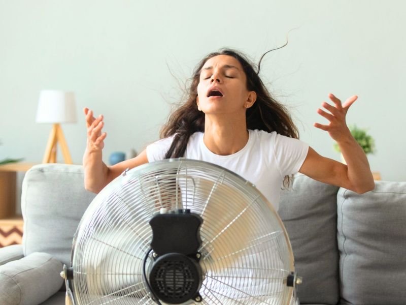 Frau kühlt sich mit einem Ventilator ab.