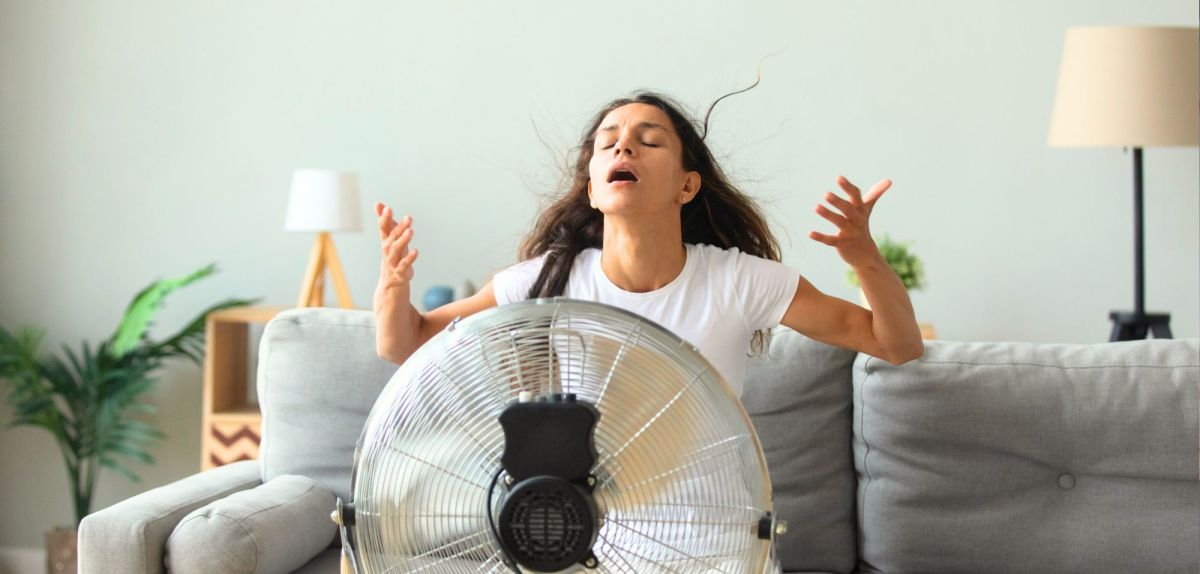 Frau kühlt sich mit einem Ventilator ab.