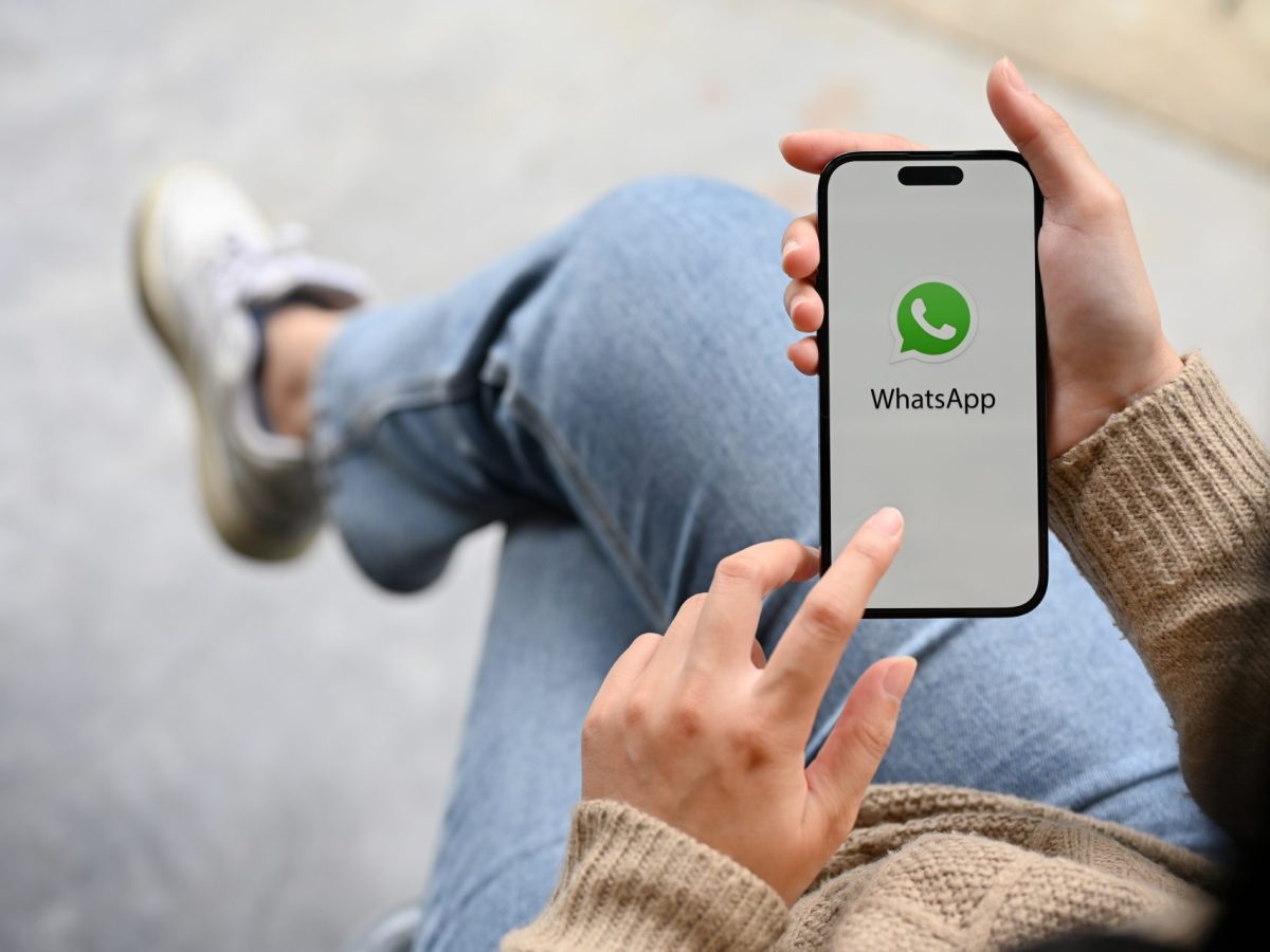 Person, die sitzt und währenddessen WhatsApp auf dem Handy öffnet.