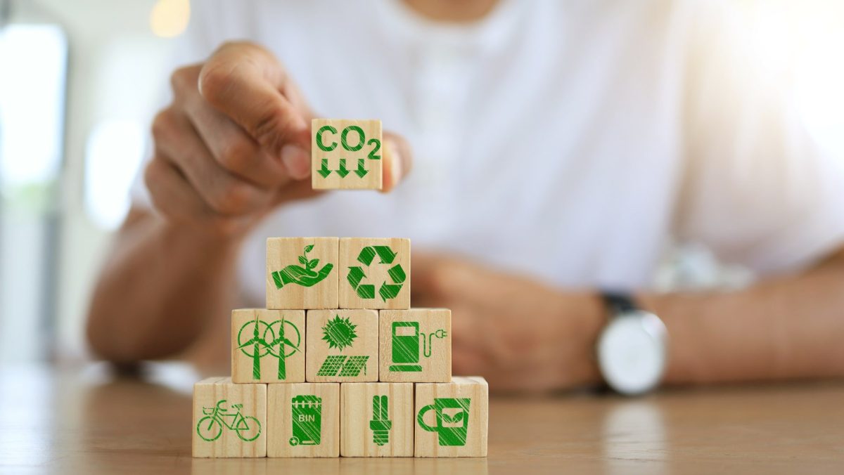 Hand stapelt Würfel mit Icons zu Umweltfragen
